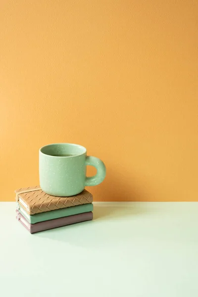 Stack of notebook and mug cup on mint green desk. orange background. copy space