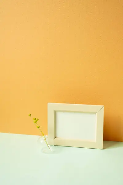 Wooden picture frame with vase of dry flower on mint green desk. orange background. copy space