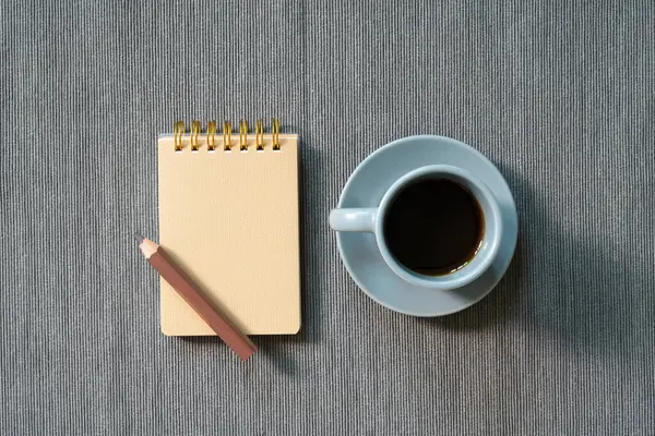 Brown notepad, colored pencil, cup of coffee on gray fabric background. top view, copy space. workspace