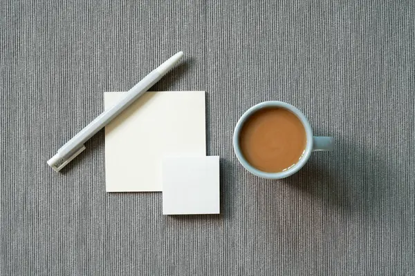 Stationery office supply. memo pad, pen, cup of coffee on gray fabric background. top view, copy space. workspace