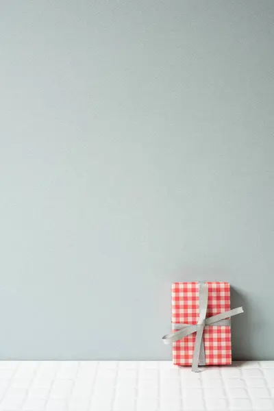 Red check pattern gift box on white tile table. gray wall background. copy space
