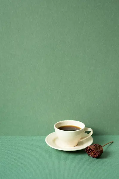 Cup of coffee with dry rose on table. green wall background. copy space