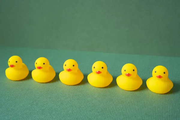 Row of yellow rubber duck doll on green background. teamwork leadership concept