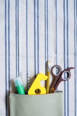 Çizgili kumaş arka plan üzerine kalem kutusuna malzeme kırtasiyesi yazmak. en üstteki görünüm
