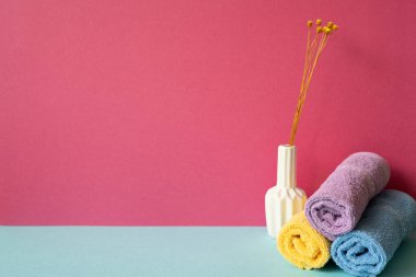 Gökyüzü mavi rafında vazo dolusu kuru çiçekli banyo havluları. pembe duvar arkaplanı