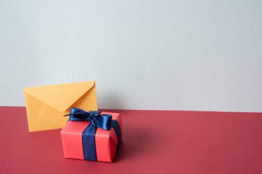 Sarı zarf ve pembe hediye kutusu kırmızı masada. gri duvar arkaplanı