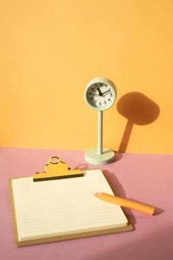 Pano ve renkli kalem, pembe masadaki saat. turuncu duvar arka planı. çalışma alanı