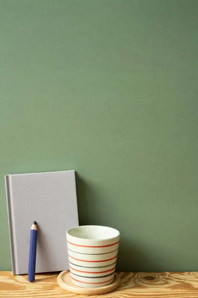 Purple diary notebook, pencil, cup on wooden desk. green wall background