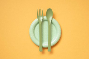 Turuncu masa arka planında boş yeşil tabak ve çatal bıçak takımı. düz yatış, üst görünüm