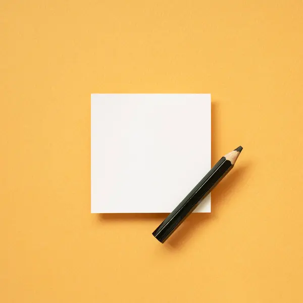 オレンジ色の机の背景に白い空白のメモ帳そして鉛筆 トップビュー コピースペース ストックフォト