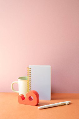 Çalışma masasında defter, bardak, kalem, bant dağıtıcısı var. pembe turuncu arkaplan