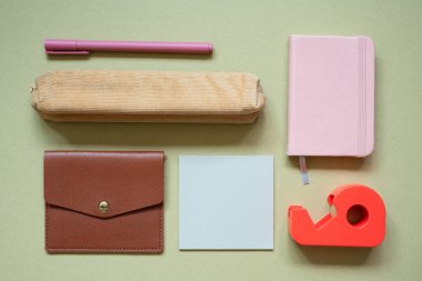 Çeşitli ofis ve okul malzemeleri. Kalem, kalem kutusu, kart cüzdanı, not defteri, not defteri, haki rengi masa arkasındaki bant dağıtıcısı. en üstteki görünüm