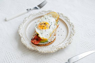 Kahvaltıda kızarmış yumurta avokado ve beyaz arka planda pastırma.