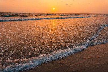 Kumsalda gün batımı ve okyanus dalgaları ve turuncu gökyüzü