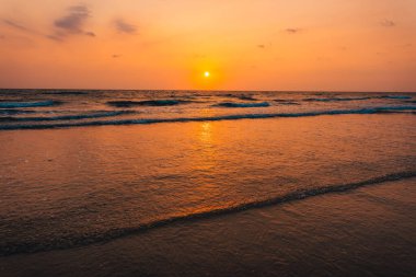 Kumsalda gün batımı ve okyanus dalgaları ve turuncu gökyüzü