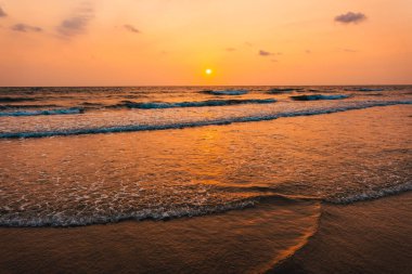 Kumsalda gün batımı ve okyanus dalgaları ve turuncu gökyüzü