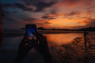 Akıllı telefon sakin kumsalın ve gökyüzünün fotoğraflarını çeker. Akşam Ao Nang, Krabi 'de, sahile git..