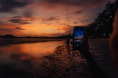 Akıllı telefon sakin kumsalın ve gökyüzünün fotoğraflarını çeker. Akşam Ao Nang, Krabi 'de, sahile git..