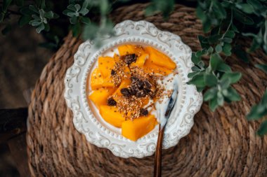 Bitkilerle dolu bir masada beyaz bir tabakta mango yoğurdu.