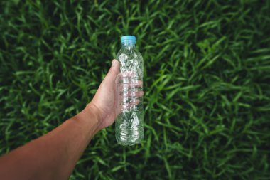 Geri dönüşüm konsepti, koyu yeşil çimlerden plastik bir su şişesi tutmak.