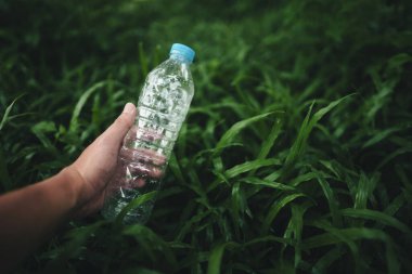 Geri dönüşüm konsepti, koyu yeşil çimlerden plastik bir su şişesi tutmak.