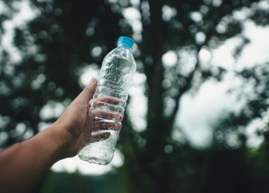 Geri dönüşüm konsepti, koyu yeşil çimlerden plastik bir su şişesi tutmak.