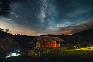 Milky Way in the night sky, wooden house in the rice field at night with stars and Milky Way in the sky clipart