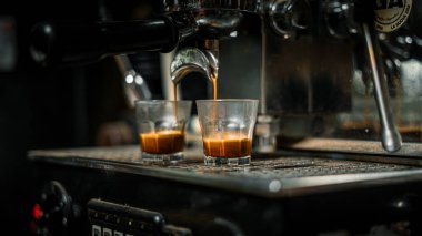Profesyonel espresso makinesi iş başında. Aynı anda küçük bardaklara iki duble koyu espresso karıştırıyor. Altın-kahverengi krema her karenin üstünde görünür.