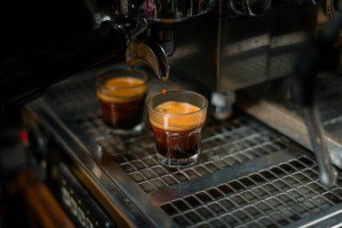 Profesyonel espresso makinesi iş başında. Aynı anda küçük bardaklara iki duble koyu espresso karıştırıyor. Altın-kahverengi krema her karenin üstünde görünür.