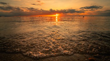 Güneş bir yaz akşamı okyanus suyunun üzerinde alçalıyordu. Turuncu ve altın ışık, su yüzeyinde ve ufukta pırıl pırıl parlıyor.