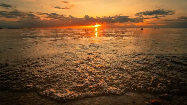 Güneş bir yaz akşamı okyanus suyunun üzerinde alçalıyordu. Turuncu ve altın ışık, su yüzeyinde ve ufukta pırıl pırıl parlıyor.