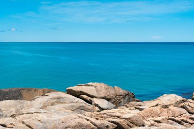 Yaz boyunca tropikal ada. Pofuduk beyaz bulutları olan parlak, masmavi bir gökyüzü ufukta süzülüyor.