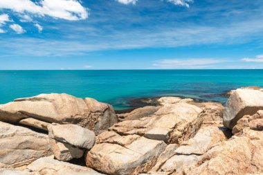 Yaz boyunca tropikal ada. Pofuduk beyaz bulutları olan parlak, masmavi bir gökyüzü ufukta süzülüyor.