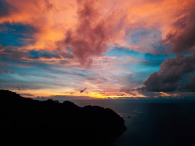 Uçsuz bucaksız okyanusun üzerinde gün batımının havadan görünüşü, canlı turuncularla boyanmış dramatik bir gökyüzünü gösteriyor.,