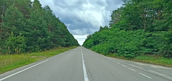 分割ストリップとアスファルトの空の高速道路 青い空に向かって緑の木々の中にいます 雨の雲のビューで道路 自動ルートは距離に入る 道路の上に雨の雲がかかっている — ストック写真