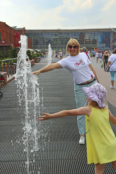happy mother with little daughter cooling about fountains. Cooling in water jets of fountains in hot summer day. Happy family spending time in city. Mother with girl in joyful mood