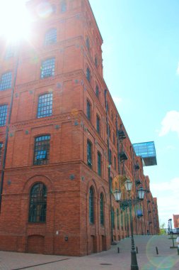 Eski tuğla bina cephesi. Polonya 'nın Lodz şehrinde pencereleri olan eski bir fabrika binası. Polonya 'da eski mimari. Kırmızı tuğla fabrikasının ön cephesi güneş ışığıyla aydınlanıyor