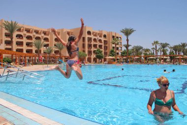 Otelde havuza atlayan küçük bir kız. Mutlu kız yaz tatilinin tadını çıkarıyor. Kız havuzdan koşuya atlıyor. Yüzme havuzunda oynayan ve yaz tatilinin tadını çıkaran bir çocuk.