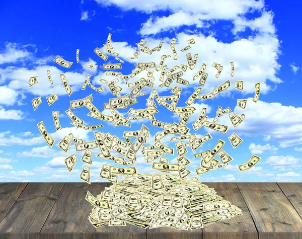 pile of dollars flying away in nature. Wind blowing bunch of dollars on wooden floor. Excessive waste of money. Money on the background of summer sky. Fabulous wealth. Money flying above wooden stand