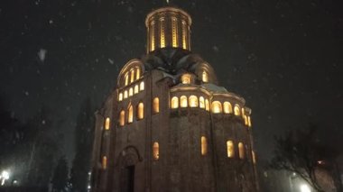 Gece gökyüzünün arka planında aydınlanmış kilise kubbeleri. Parlak fenerlerle dolu kış parkı. Kar yağarken boş park. Chernihiv 'deki Pyatnytska kilisesinde aydınlandı. Gece aydınlatma kilisesi.