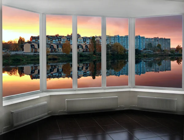 Panoramic window with view of red sunset above city buildings. Evening cityscape. Beautiful view from room window. Chimneys with smoke over the evening city. Twilight in city