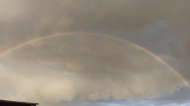 Bright rainbow in sky with clouds. Rainbow after rain. Colored rainbow above forest and field. Natural landscape. Summer scenery. Thunder storm clouds over wheat field. Cloudy sky