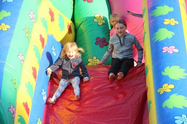 Çocuklar şişme kayağa binerler. Mutlu bir çocukluk. Neşeli çocuklar. Çocuklar eğlensin. Küçük kız kardeşler oyun alanında oynuyorlar.