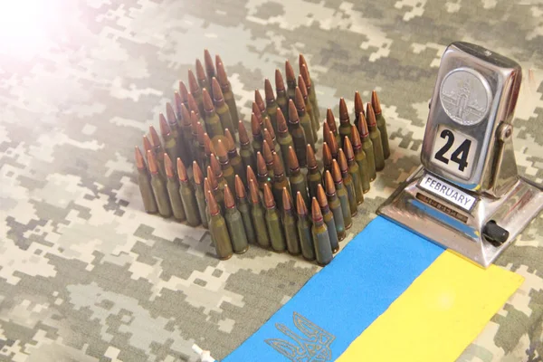 coat of arms of Ukraine laid out from cartridges on background of camouflage clothing and dark sky. Cartridges for Kalashnikov assault rifle. War Concept. Ukrainian national symbol