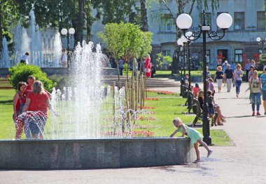 Chernihiv-Ukrayna. 14 Temmuz 2018: Şehir çeşmelerinde suya dokunmaya çalışan küçük bir kız. İnsanlar şehir parkında fıskiyeli dinleniyor. Güneşli bir yaz günü. Çocuk şehir çeşmesinin suyuyla oynuyor. Yaşam tarzı kavramı