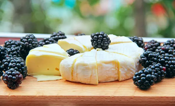 Cheese with blueberries on a wooden board. Sliced cheese with berries. blackberries with cheese. Natural food. Black berries on the board. Lunch with eco products in the garden