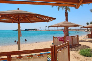 Deniz kıyısındaki tatil. Şemsiyeler. Palmiye ağaçları, kum ve kumlu sahil manzaralı tropik bir tatil köyü. Rahatlama yeri. Dinlenme yeri. Kızıl deniz rahatla. Cennet Kızıl Deniz 'in kıyısında dinleniyor. Tatil kavramı