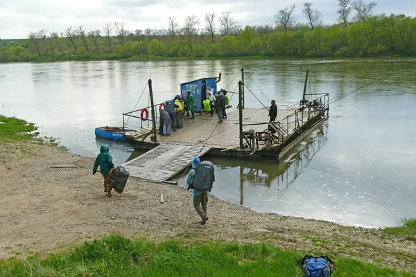 Turistler nehri geçiyor. Nehrin karşısındaki kırsal bir feribot insan, araba ve kargo taşıyor. Turistler feribotun nehrin diğer tarafına geçmesini bekliyorlar..