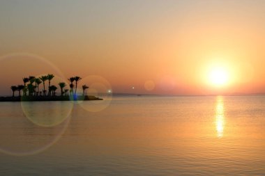 Tropikal Resort egzotik tatil. Tropikal adada şafak. Palmiye ağaçları ile deniz ve ada üzerinde günbatımı. Parlak şafağın arka planda adada palmiye ağaçlarının siluetleri. Okyanusun üzerinde parlak güneş