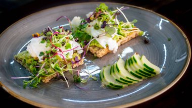 a healthy breakfast of poached eggs with avocado on toast and garnished with sliced cumber